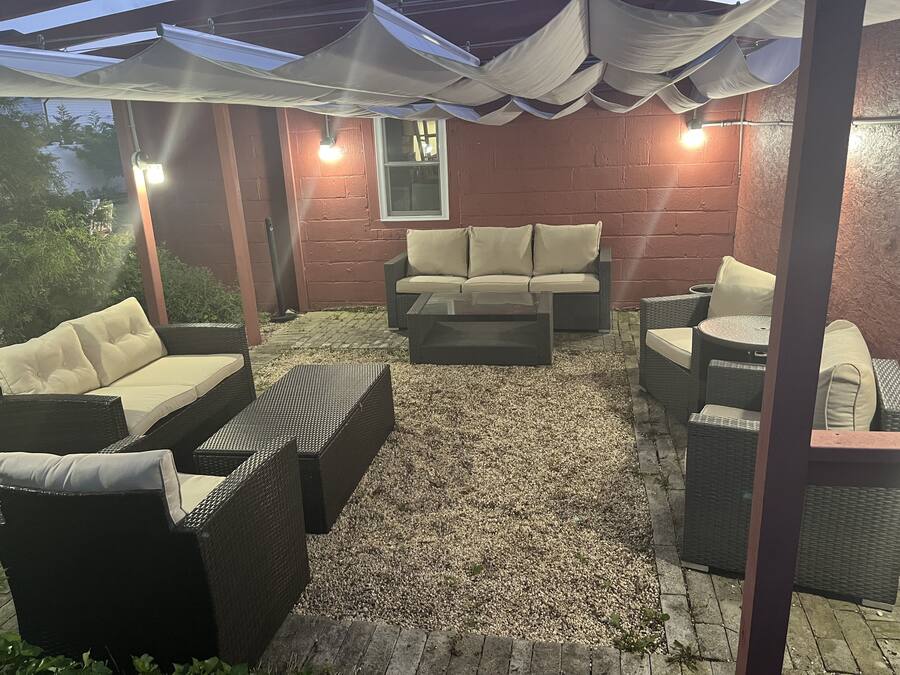An outdoor patio area with wicker furniture, a stone floor, and a pergola with lights.
