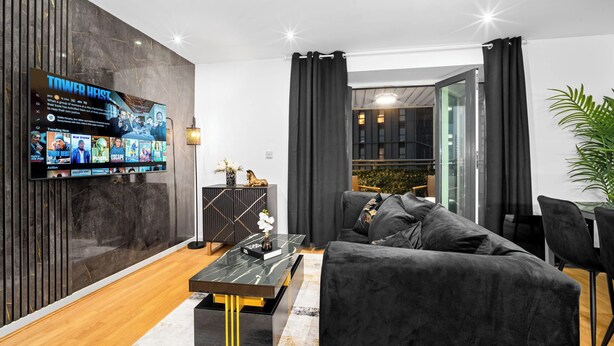 Ein modernes Wohnzimmer mit einem Flachbildfernseher, dunklen Sofas, einem Couchtisch und einem Essbereich.