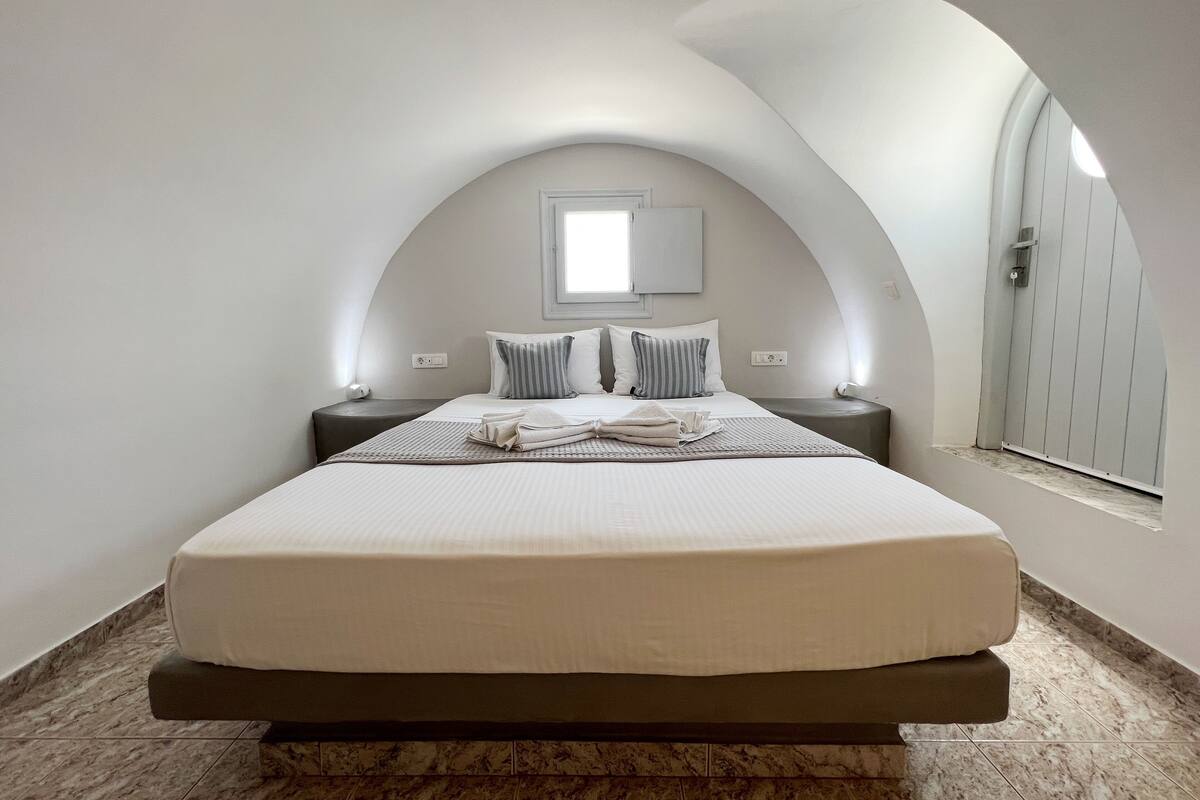 Une chambre à coucher avec un grand lit, deux tables de chevet, une commode, une fenêtre et une porte.