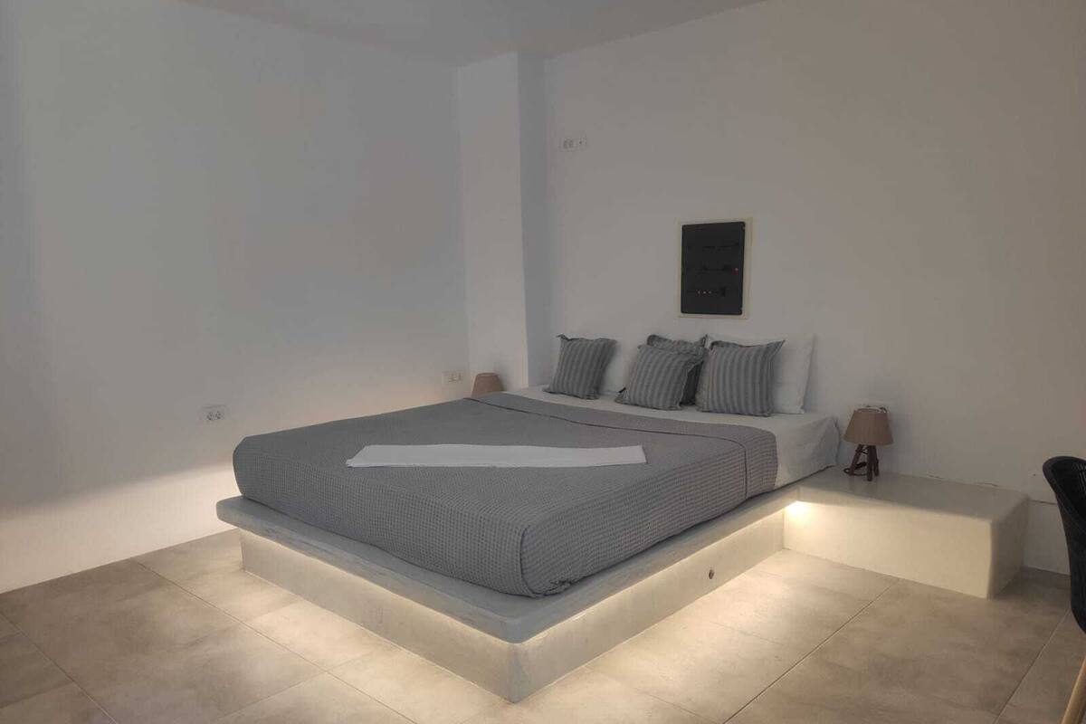 Une chambre moderne avec un grand lit, une table de chevet, une lampe et un panneau de commande fixé au mur.