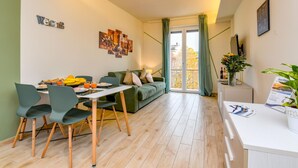 A modern living room with a dining area, a sofa, and a coffee table. There is a view of the outside through a large window. - Appartamento Ulivo in Sal (Salò)