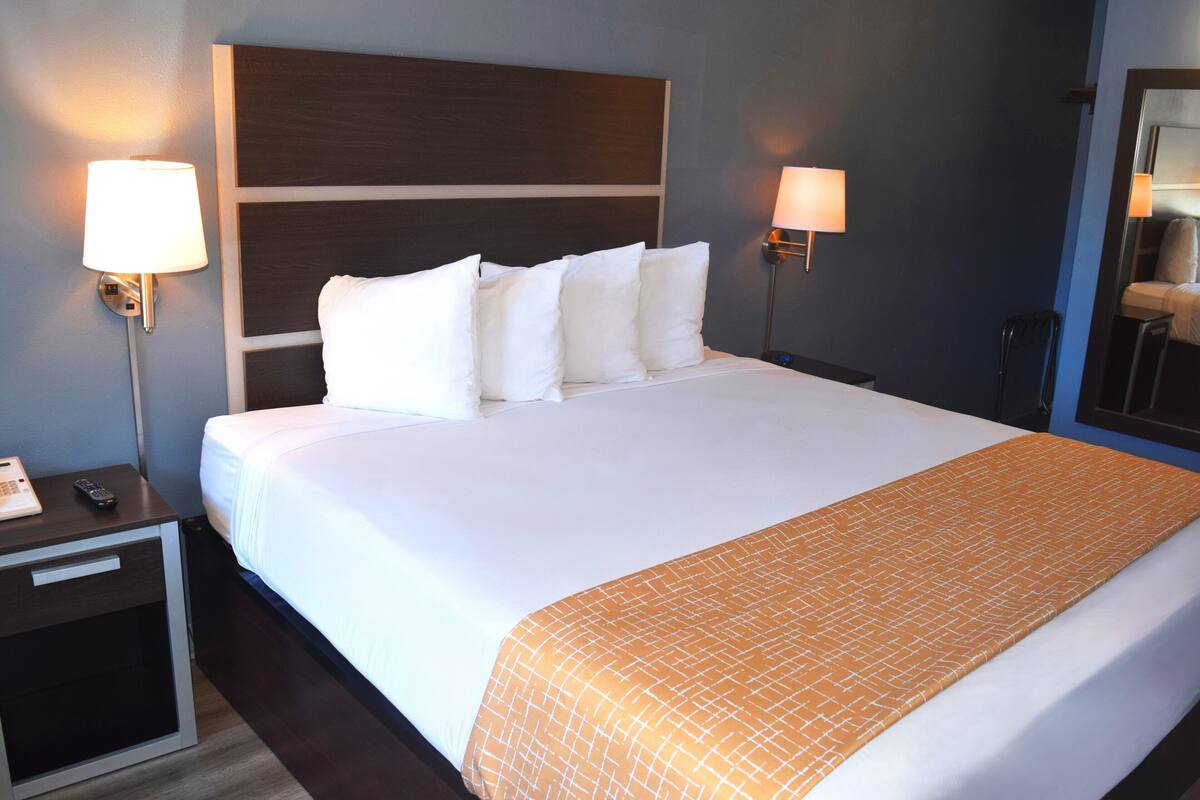 A hotel room with a large bed, two bedside lamps, a nightstand, and a mirror.