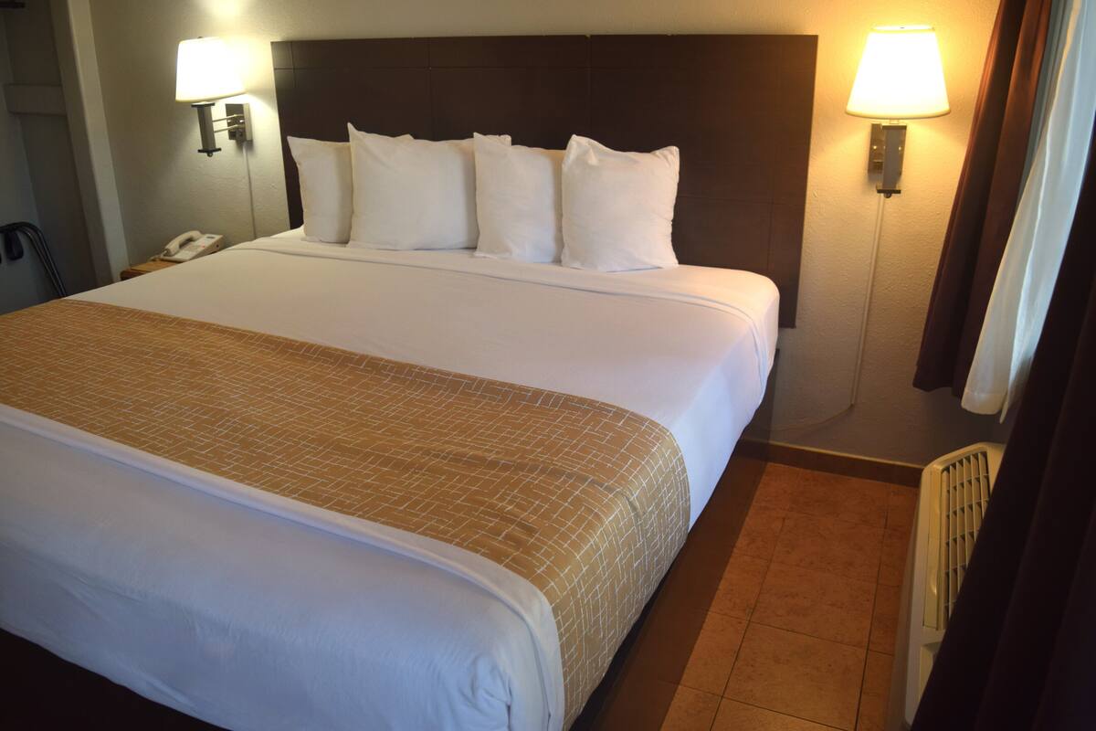 A hotel room with a large bed, two bedside lamps, a telephone, and a radiator.