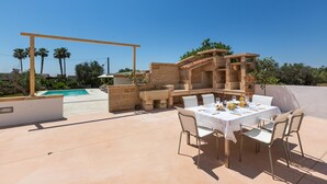 Un patio exterior con una barbacoa de piedra, una piscina y una mesa lista para comer.