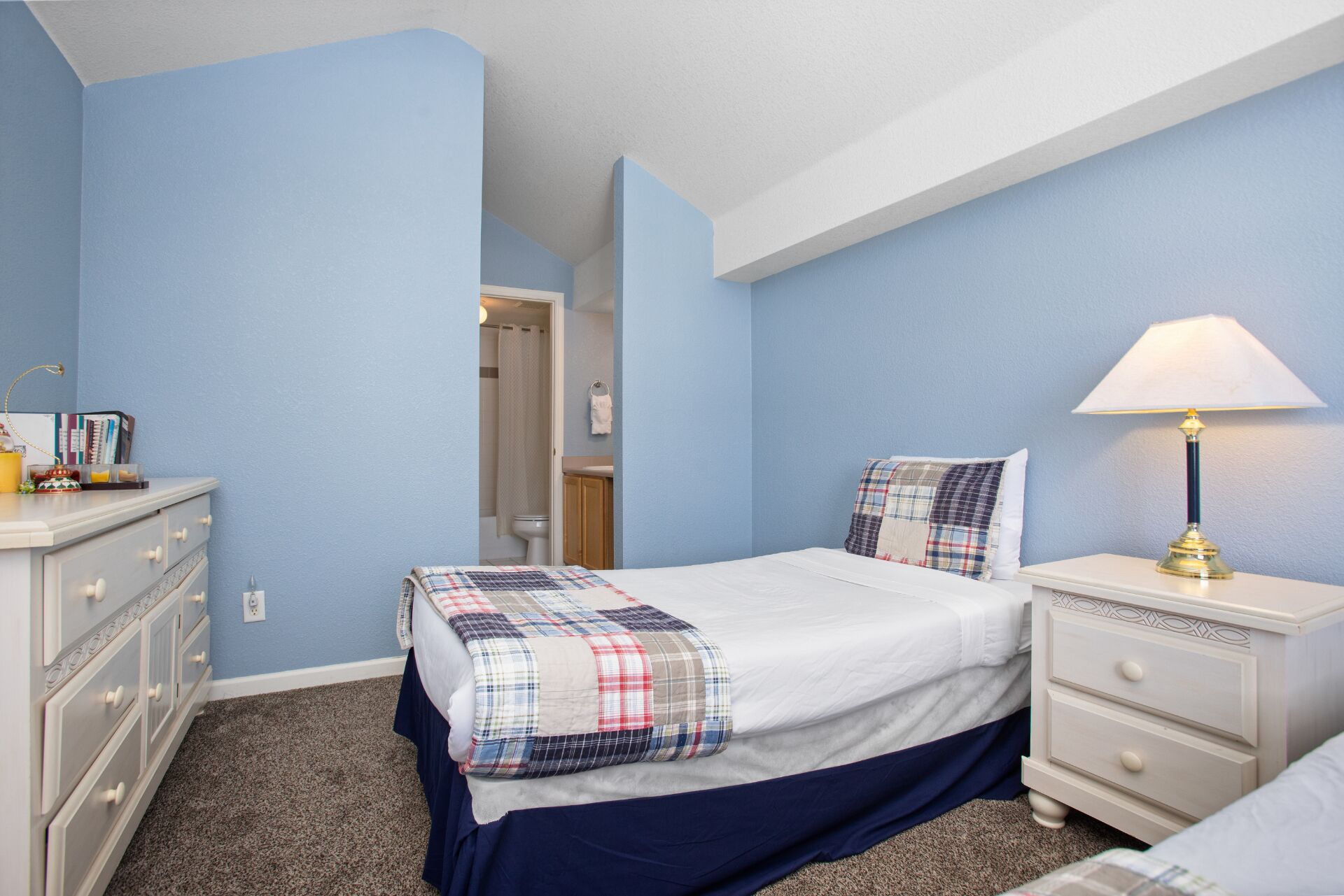 A bedroom with a bed, a nightstand, a dresser, and a bathroom visible through an open door.