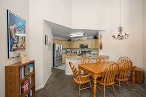 A compact kitchen with modern appliances, a dining area with wooden chairs, and a bookshelf with books.