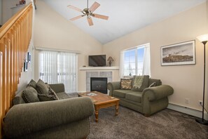 A living room with a fireplace, two sofas, a coffee table, a TV, and a ceiling fan.