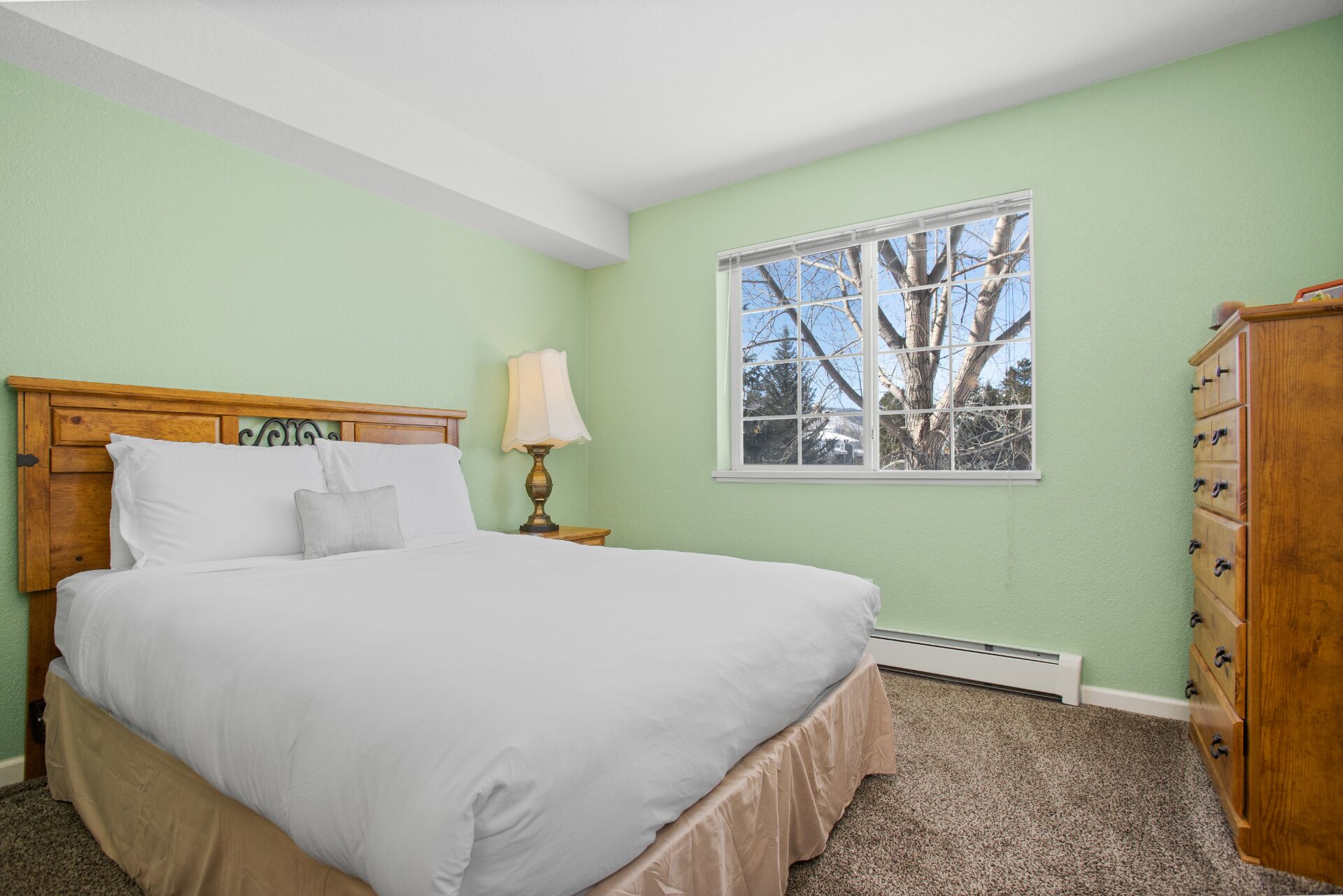 Une chambre à coucher comprenant un lit, une table de chevet, une lampe, une fenêtre et une commode.