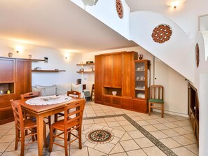 Una sala acogedora con una mesa de comedor de madera, sillas y un sofá. Hay un mueble de madera grande con estantes, una mesita con un jarrón y un adorno en la pared.