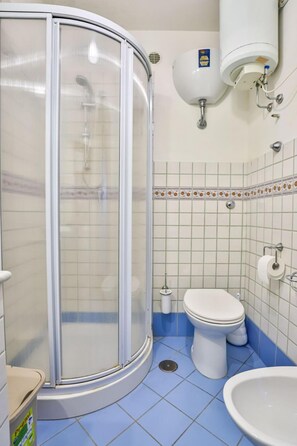 Un baño con cabina de ducha, inodoro, lavamanos y calentador de agua.