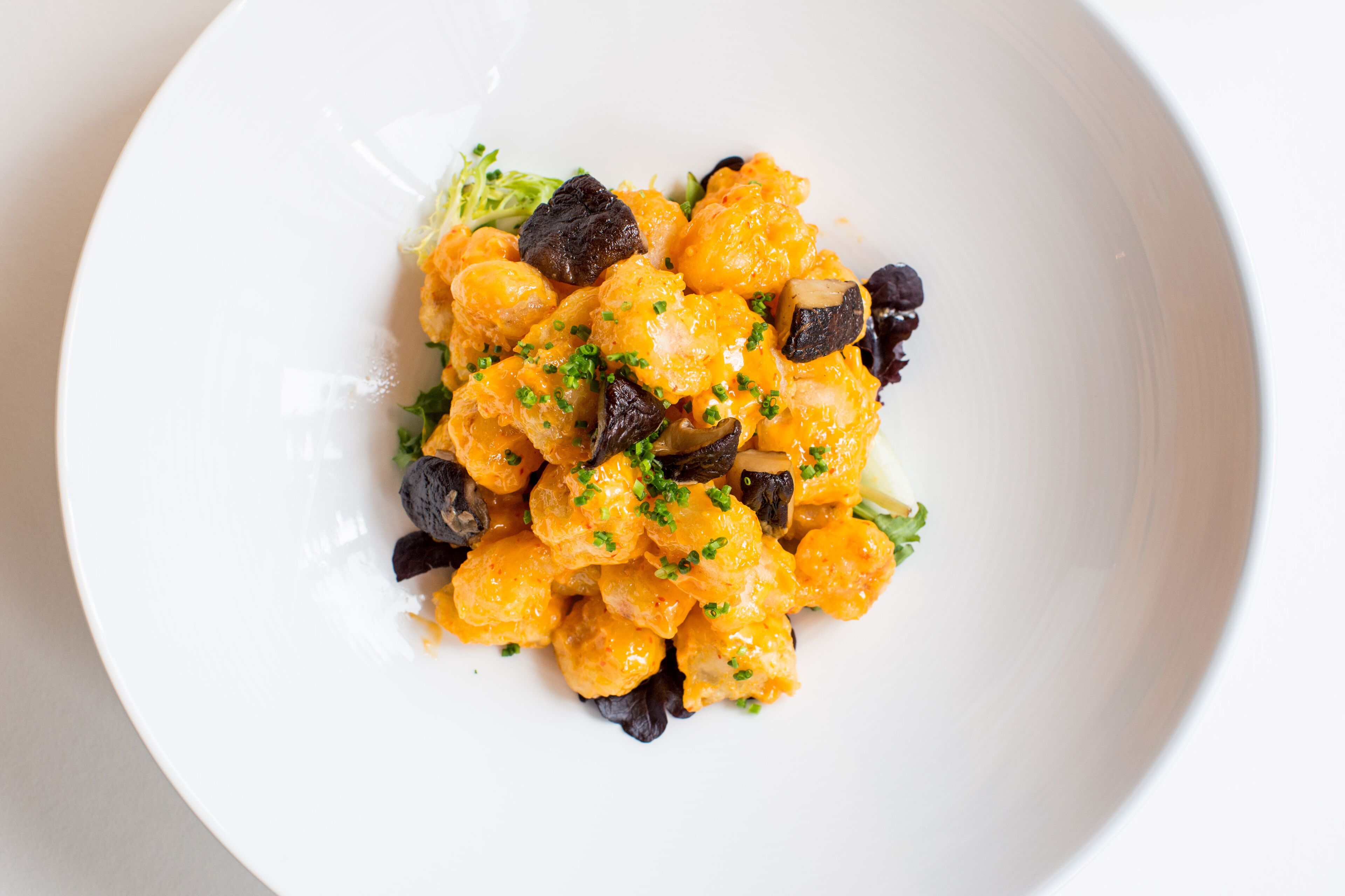 A white plate with a dish of orange-colored food, possibly cheese or a similar item, garnished with green herbs.
