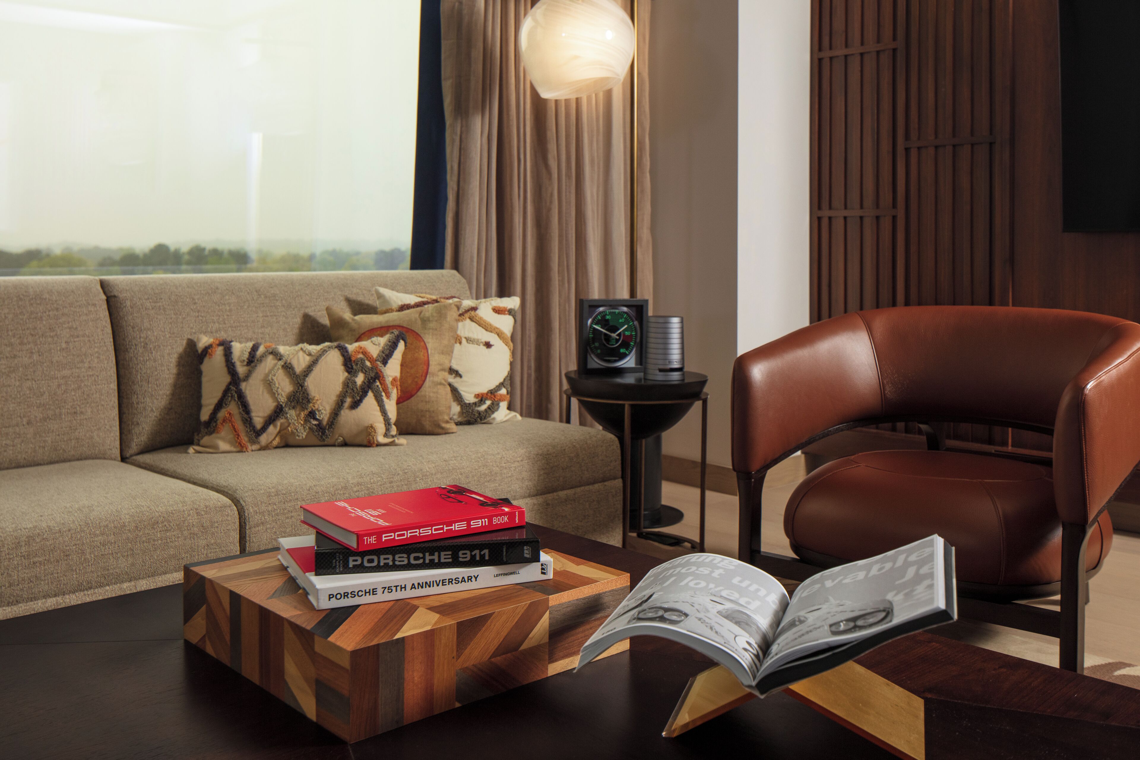 Una sala moderna con un sillón de cuero, un sofá con cojines estampados, una mesa de centro con libros y una mesita de noche con una lámpara.