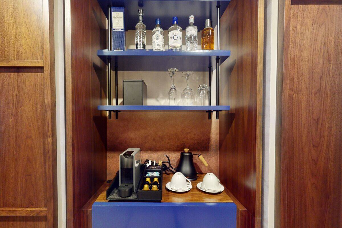 A minibar with liquor bottles, glasses, and a coffee machine.