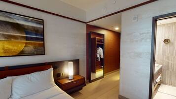 A hotel room with a bed, a nightstand with a lamp, a mirror, and a bathroom with a sink and toilet.