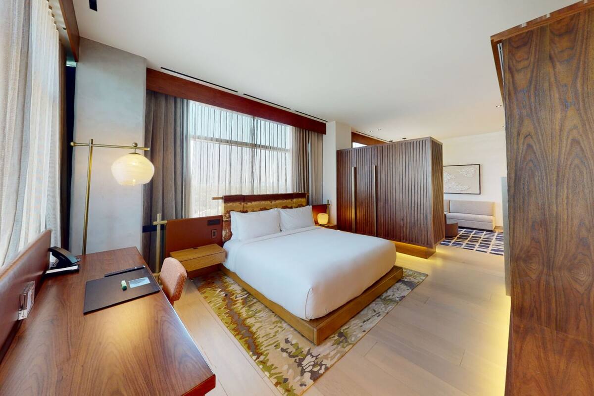 A modern hotel room with a large bed, a desk, a wardrobe, and a window with curtains.