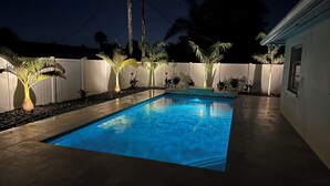 Una piscina rectangular con agua azul cristalina, rodeada por una cerca blanca y diversas plantas en macetas.