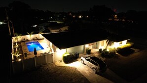 Una propiedad residencial de noche con piscina, patio cubierto y un coche en la entrada.