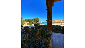 Vista di una zona piscina con cielo azzurro, circondata da vegetazione e una struttura a pergola.