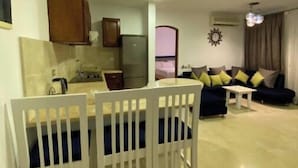 Un soggiorno con divano, un tavolo da pranzo con sedie, una zona cucina con pensili e frigorifero, e una lampada a soffitto.