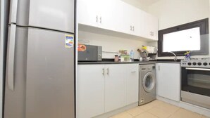 Een kleine keuken met een koelkast, wasmachine, oven en een raam.