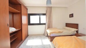 Een slaapkamer met een bed, een kledingkast, een raam en een hanglamp.