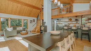 Un vaste espace de vie comprenant une grande table à manger en bois, un canapé et une cuisine à l’arrière-plan.