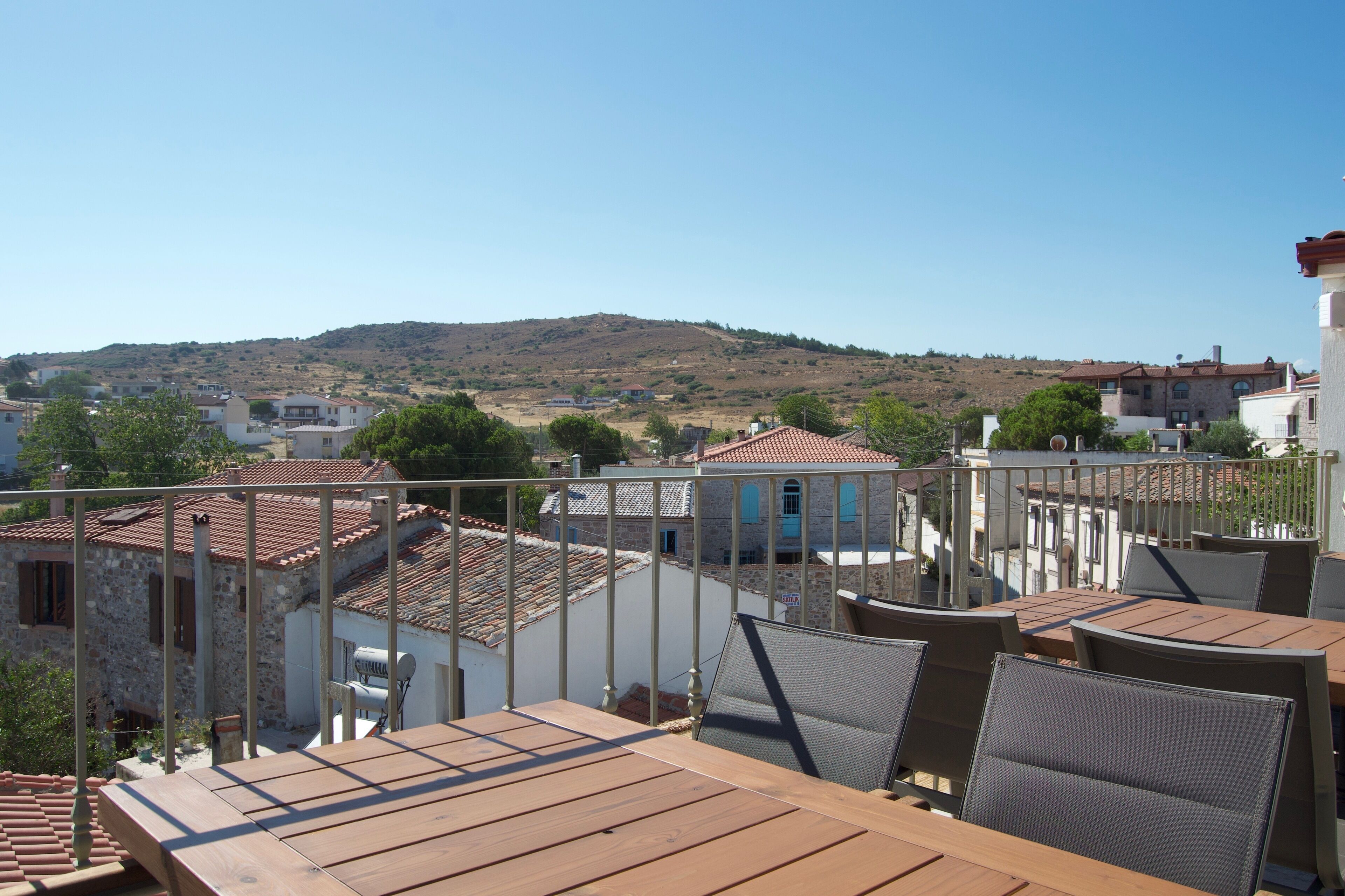 A terrace with wooden tables and chairs, overlooking a hillside with buildings.