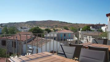 A terrace with wooden tables and chairs, overlooking a hillside with buildings.
