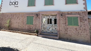 A building with a white facade, green shutters, and a cobblestone ground. - Boja Küçükköy (Ayvalik)