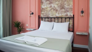 A hotel room with a bed, a headboard with a floral pattern, a small plant, and a nightstand with a lamp. - Boja Küçükköy (Ayvalik)