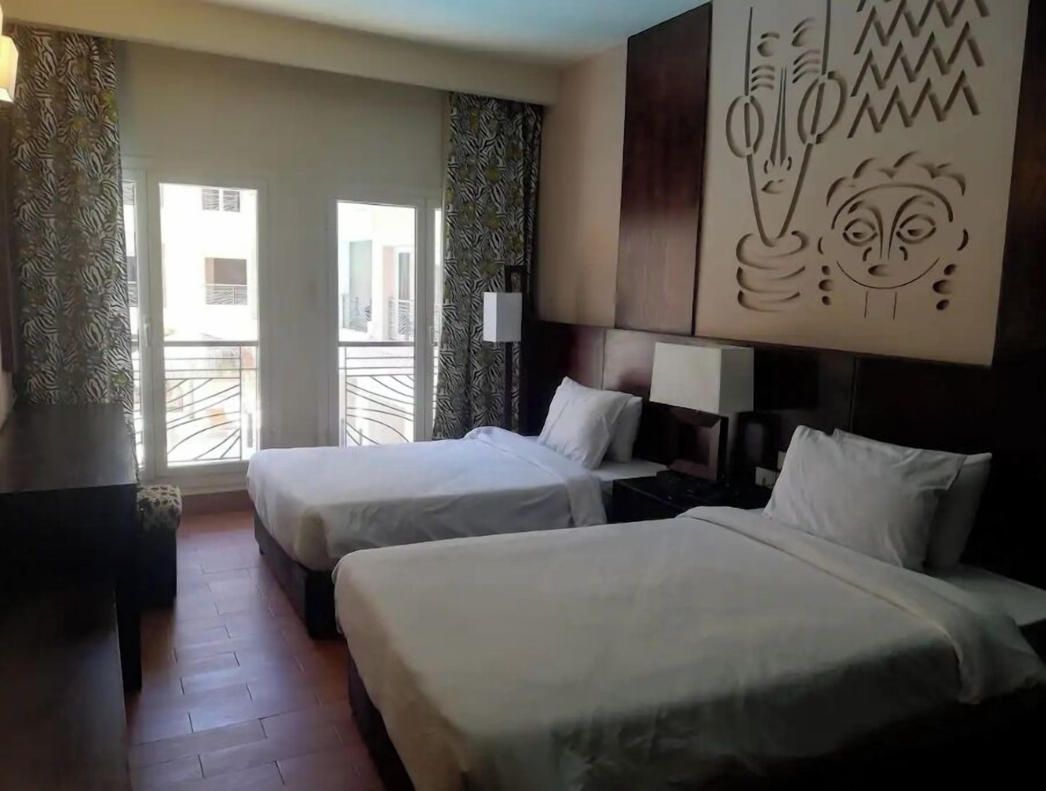 A hotel room with two beds, a large window, and a decorative wall piece.
