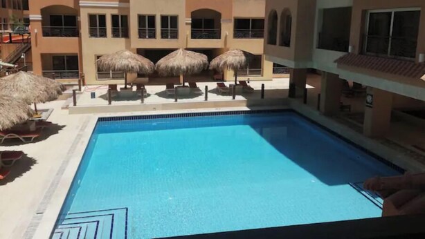A swimming pool with a clear blue water surface, surrounded by lounge chairs and thatched umbrellas. - 2 bedroom & breakfast in The Bosque Hotel Hurghada (Red Sea Governorate)