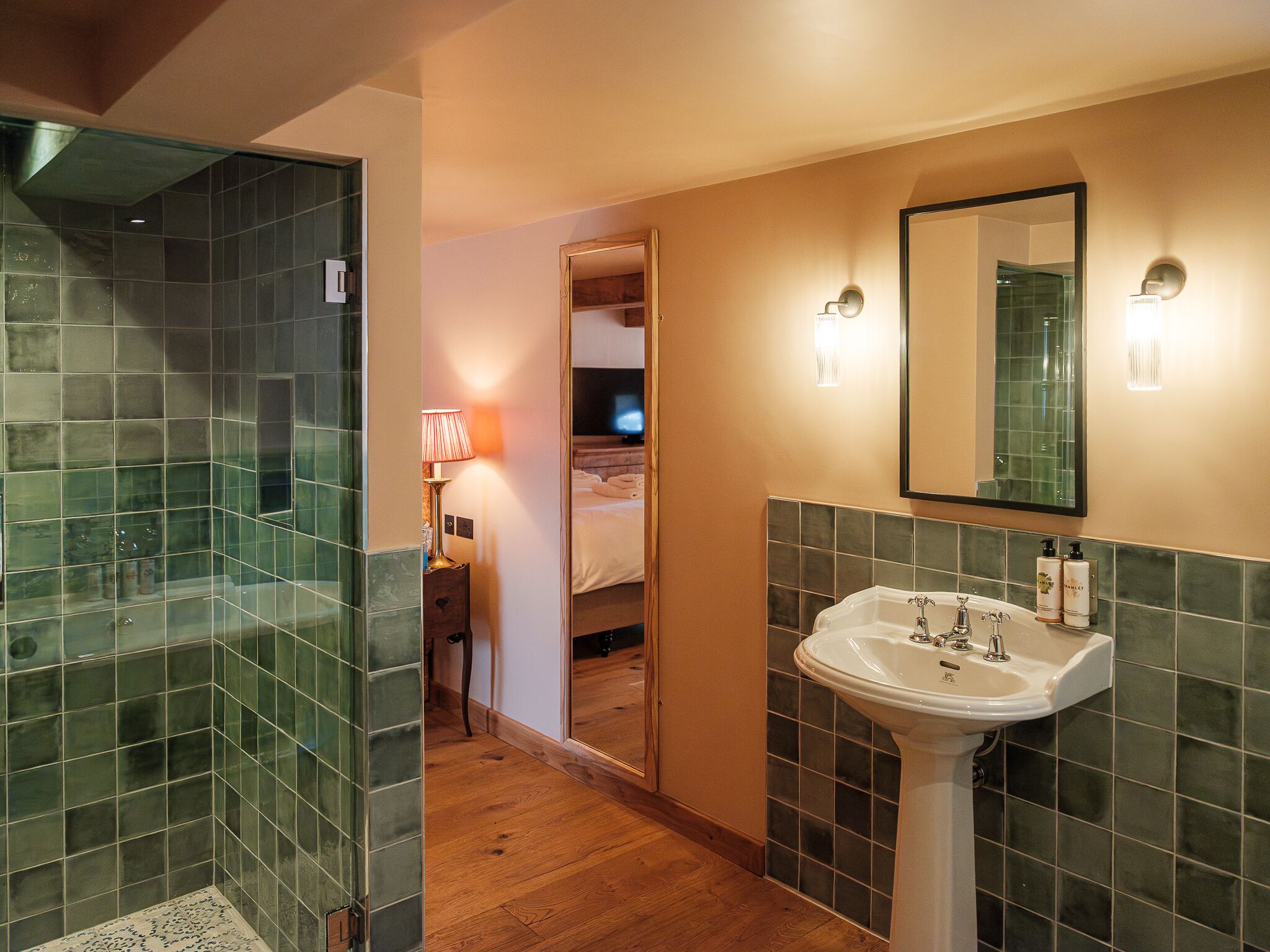A bathroom with a glass shower enclosure, a sink with a mirror, and a wooden floor.