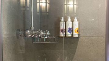 A glass-enclosed shower with a rain showerhead, a chrome faucet, and a shelf with toiletry bottles.
