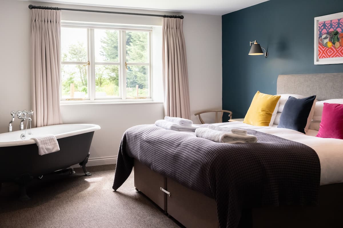 A modern bedroom with a large bed, a bathtub, and a window with curtains.