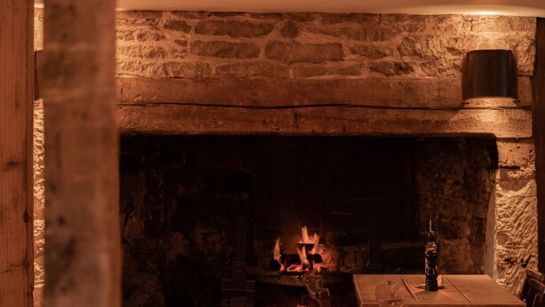 Una chimenea de piedra con fuego, una mesa de madera y una silla en una habitación rústica.