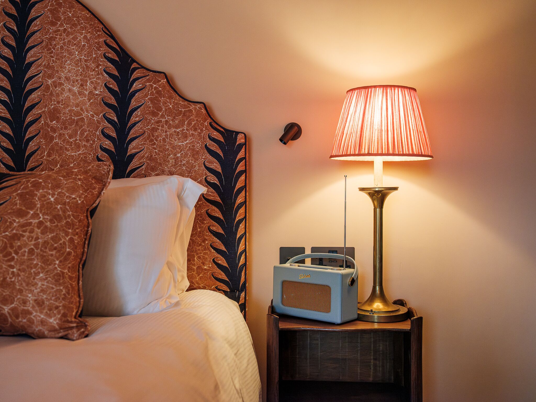 A bed with a patterned headboard, a bedside lamp, and a radio on a wooden nightstand.