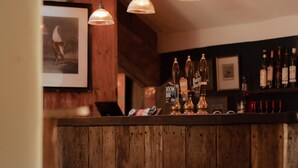 Zona de bar con taburetes de madera, iluminación colgante y una variedad de botellas de licores.