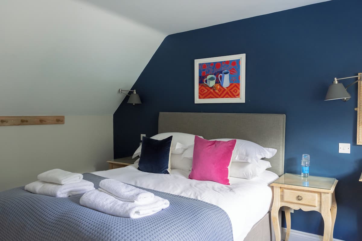 A neatly made bed with white and blue bedding, a blue wall, and a framed artwork above the bed.