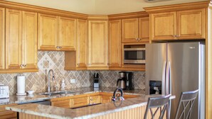 A kitchen with wooden cabinets, a central island with bar stools, a stainless steel refrigerator, and a ceiling fan. - Big Sky Villa: sunset view; great for large families; pool; back up power  (St. John USVI)