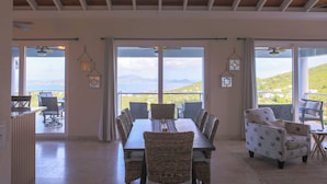 A dining area with a table and chairs, large windows with curtains, and a view of the landscape. - Big Sky Villa: sunset view; great for large families; pool; back up power  (St. John USVI)