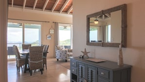 A dining area with wicker chairs, a wooden table, and a gray cabinet with drawers. - Big Sky Villa: sunset view; great for large families; pool; back up power  (St. John USVI)