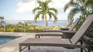 A poolside area with lounge chairs and a view of palm trees and the ocean. - Big Sky Villa: sunset view; great for large families; pool; back up power  (St. John USVI)