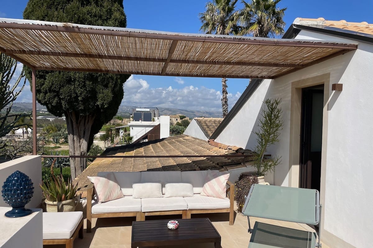 Un área de estar al aire libre cubierta con sofá y sillones, una mesa y vistas del paisaje circundante.