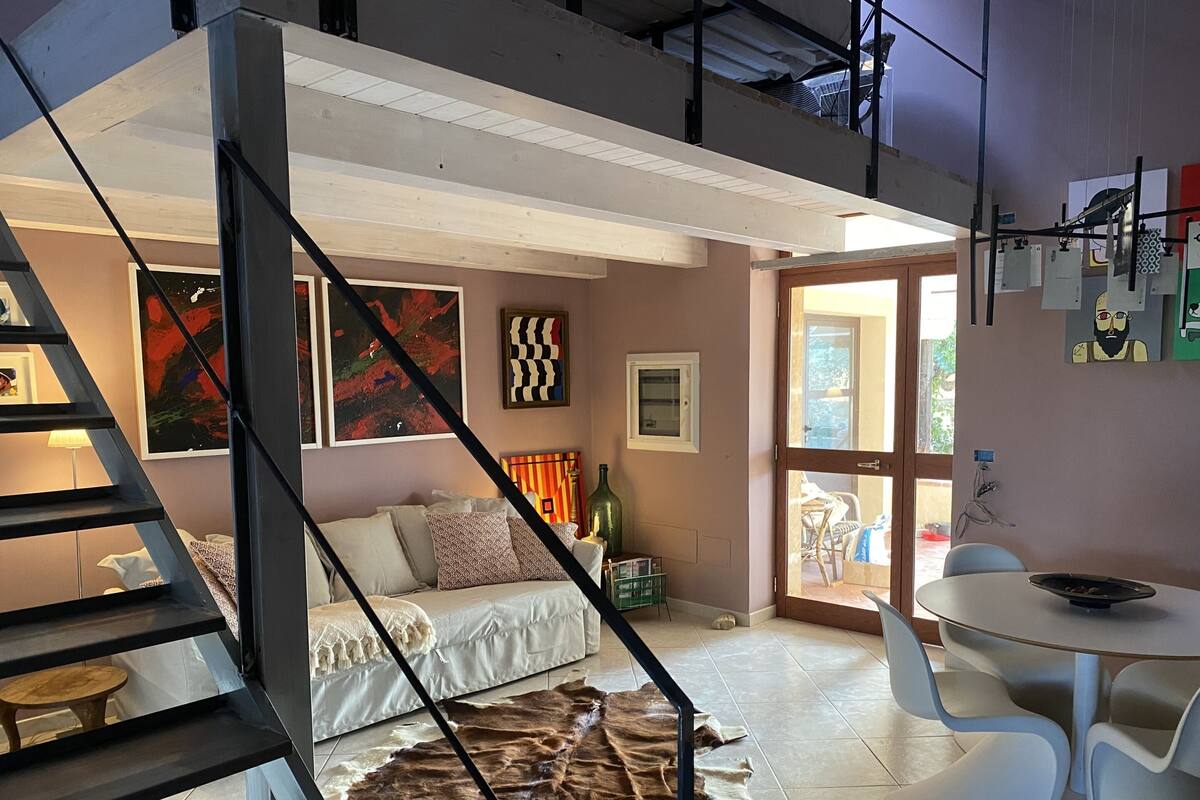 Un interior moderno con una escalera, un sofá, una mesa de comedor y obras de arte en las paredes.