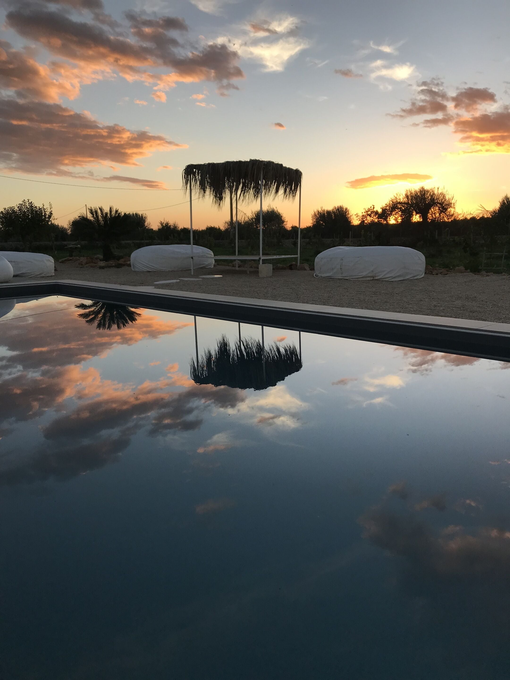 Un entorno tranquilo al aire libre con un estanque reflectante, zonas de estar cubiertas y vistas al atardecer.