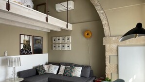 Una sala moderna con un sofá seccional gris, una mesa de centro de vidrio transparente, un sillón azul y una lámpara colgante.