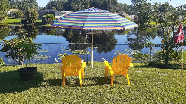 Two yellow chairs facing a pond with a striped umbrella and a flag in the background. -  Homey Work and Play Private Suite in Citrus Park! (Tampa)