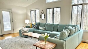 A living room with a green sofa, a wooden coffee table, and a vase of flowers. - Hosts groups up to 13; relax with the whole crew at this private, peaceful getaway (Afton)