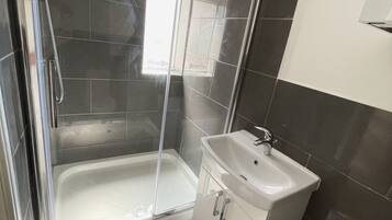 A modern bathroom with a glass-enclosed shower, a white sink, and dark tiled walls.